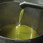 Demonstrating the process of making homemade olive oil by pouring it into a metal pot.