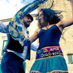 A man and a woman performing an energetic Italian folk dance in front of a building.