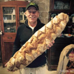 A man holding up a large loaf of bread while listening to Italian folk music.