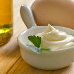 A bowl of sour cream and MAYO on a wooden table.